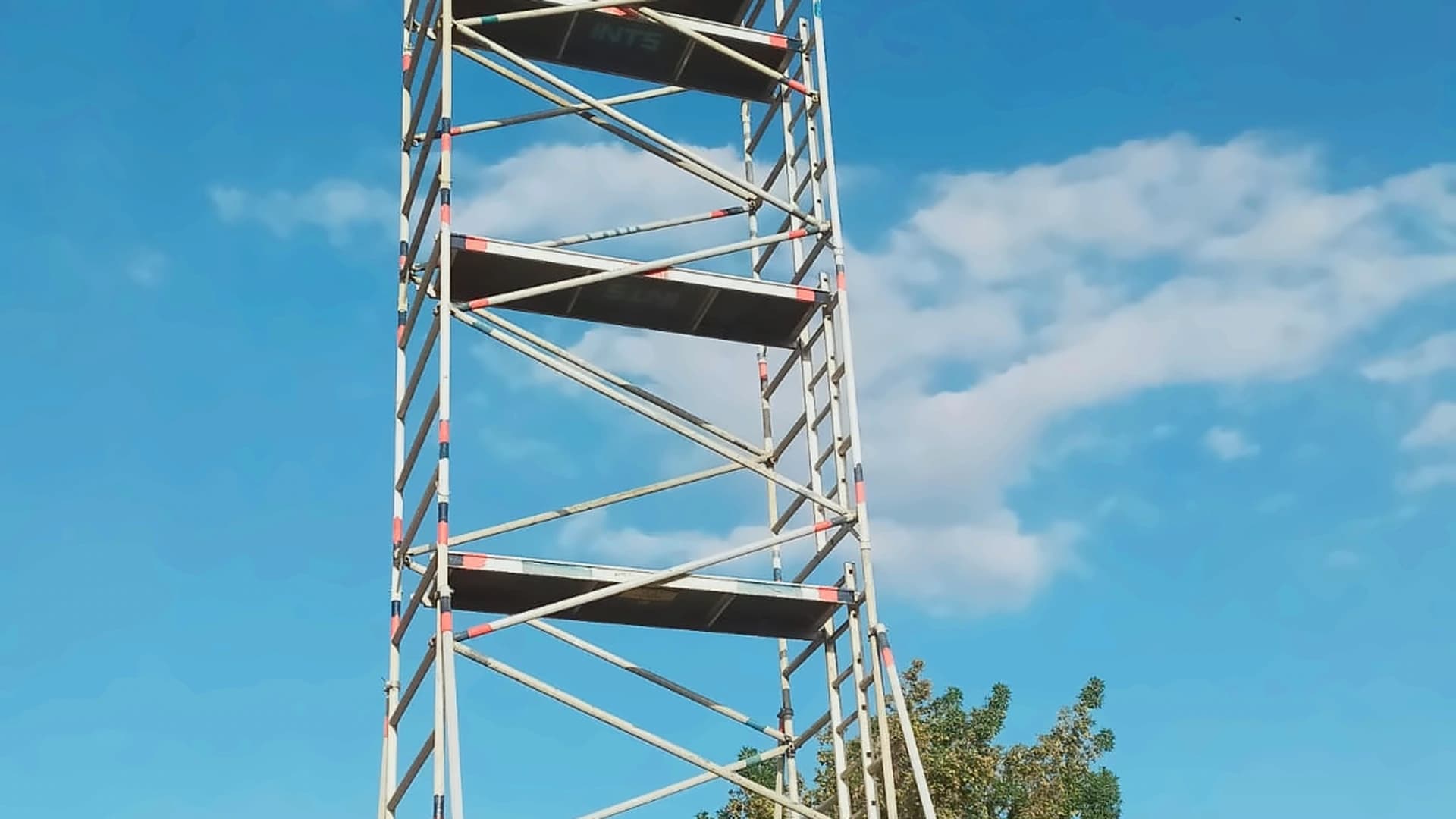 Tall scaffold access tower with working platforms and diagonal bracing under a blue sky
